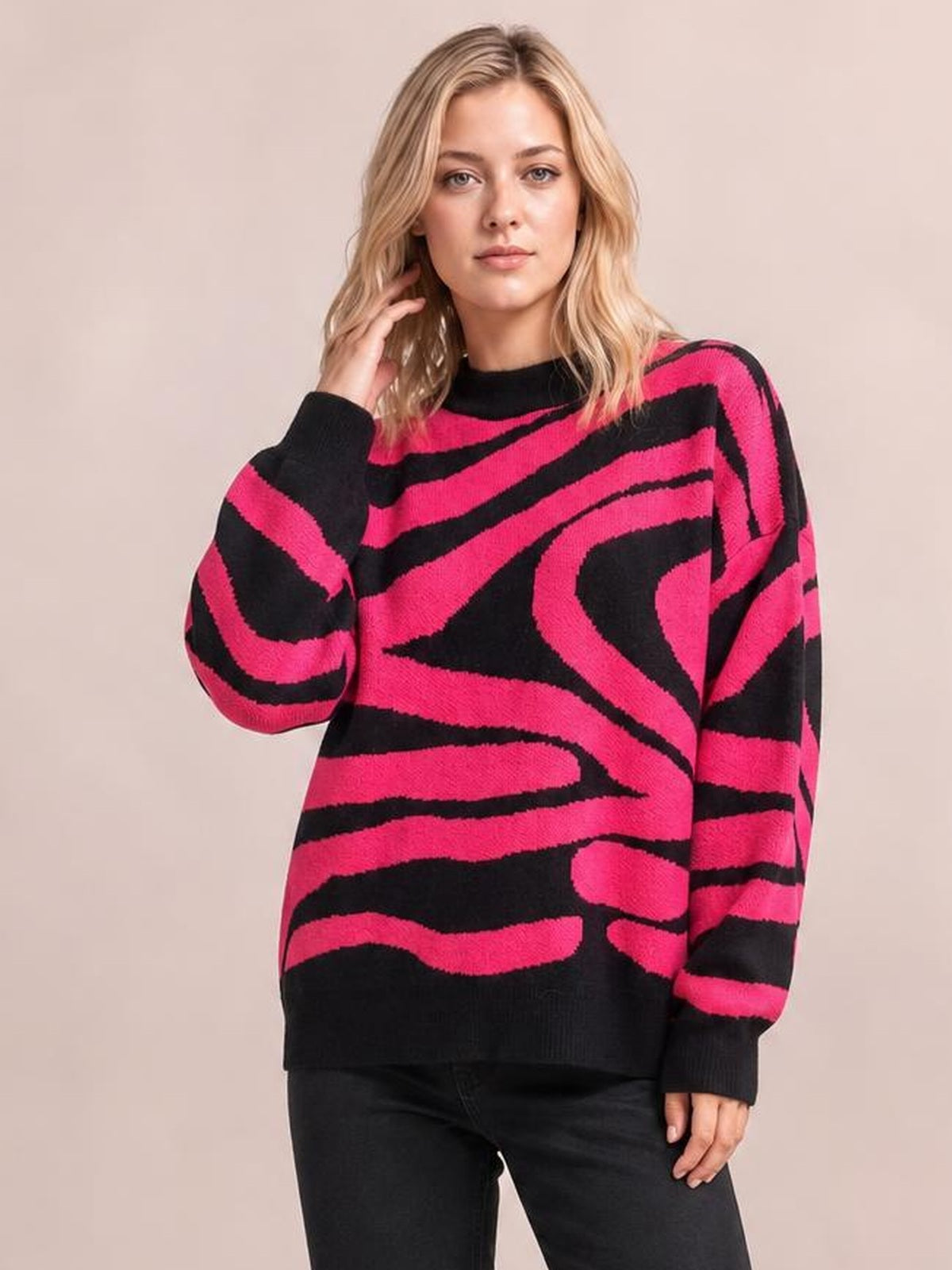 Model wearing an oversized pink and black zebra print round neck sweater with long sleeves, ribbed cuffs and hem, posing with one hand in her hair.