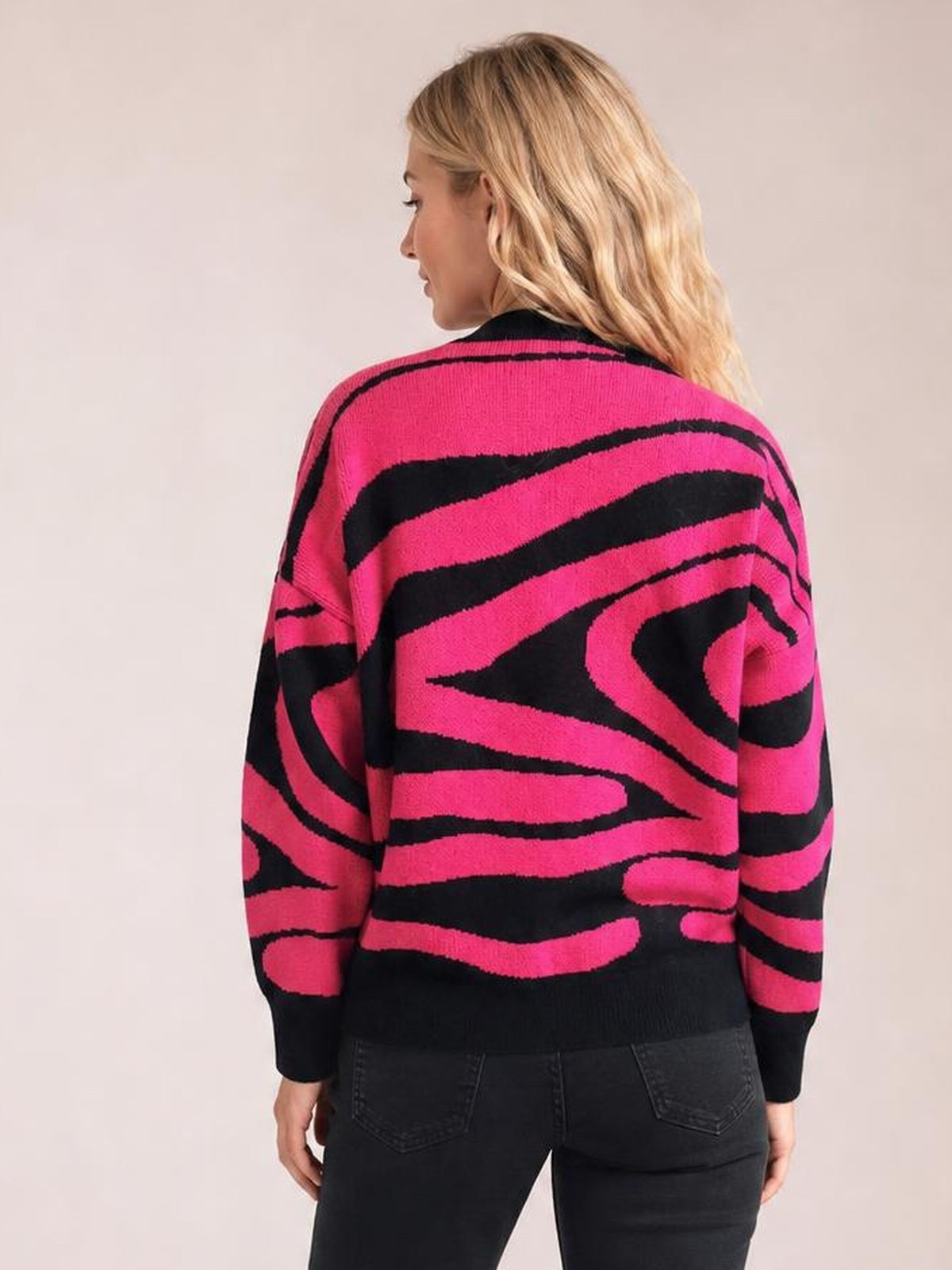 A model stands turned away in an oversized hot pink and black zebra print sweater with a round neck, long sleeves, and ribbed cuffs and hem.