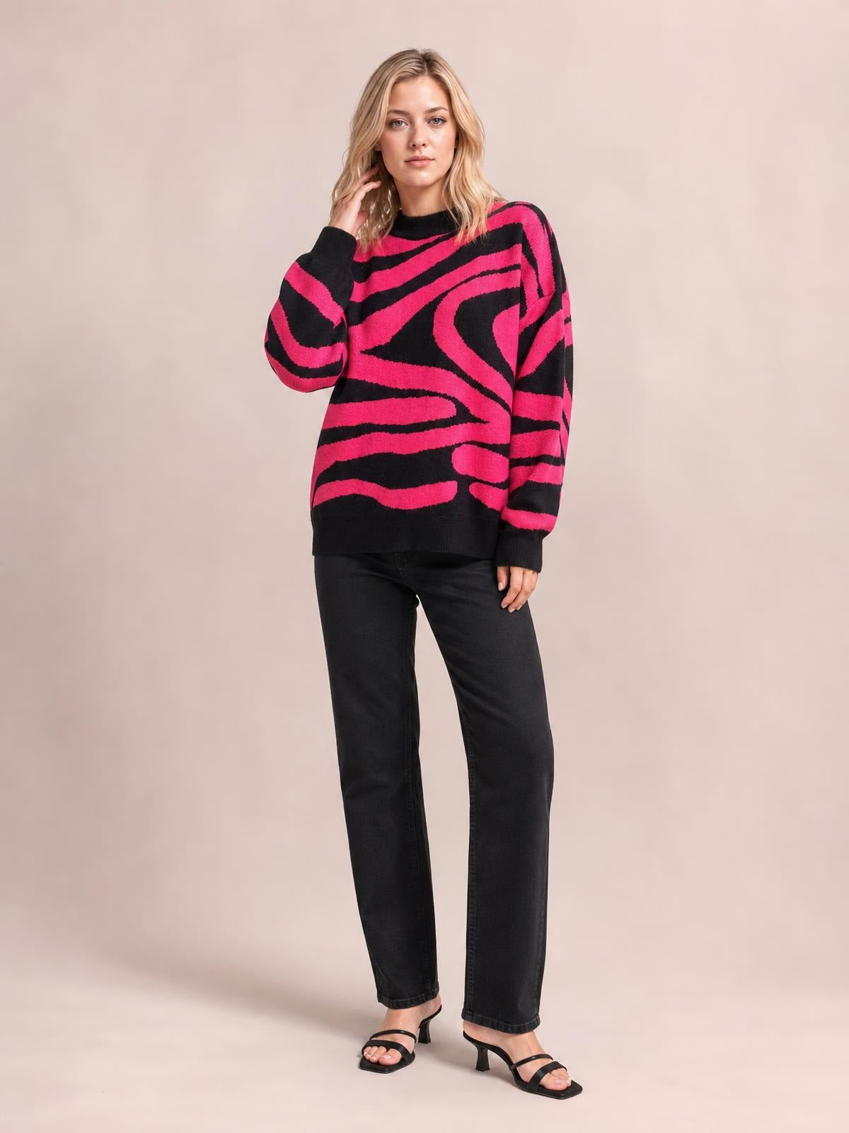 Model wears an oversized pink and black zebra print round neck sweater with long sleeves, ribbed trim, and a relaxed silhouette while touching her hair.