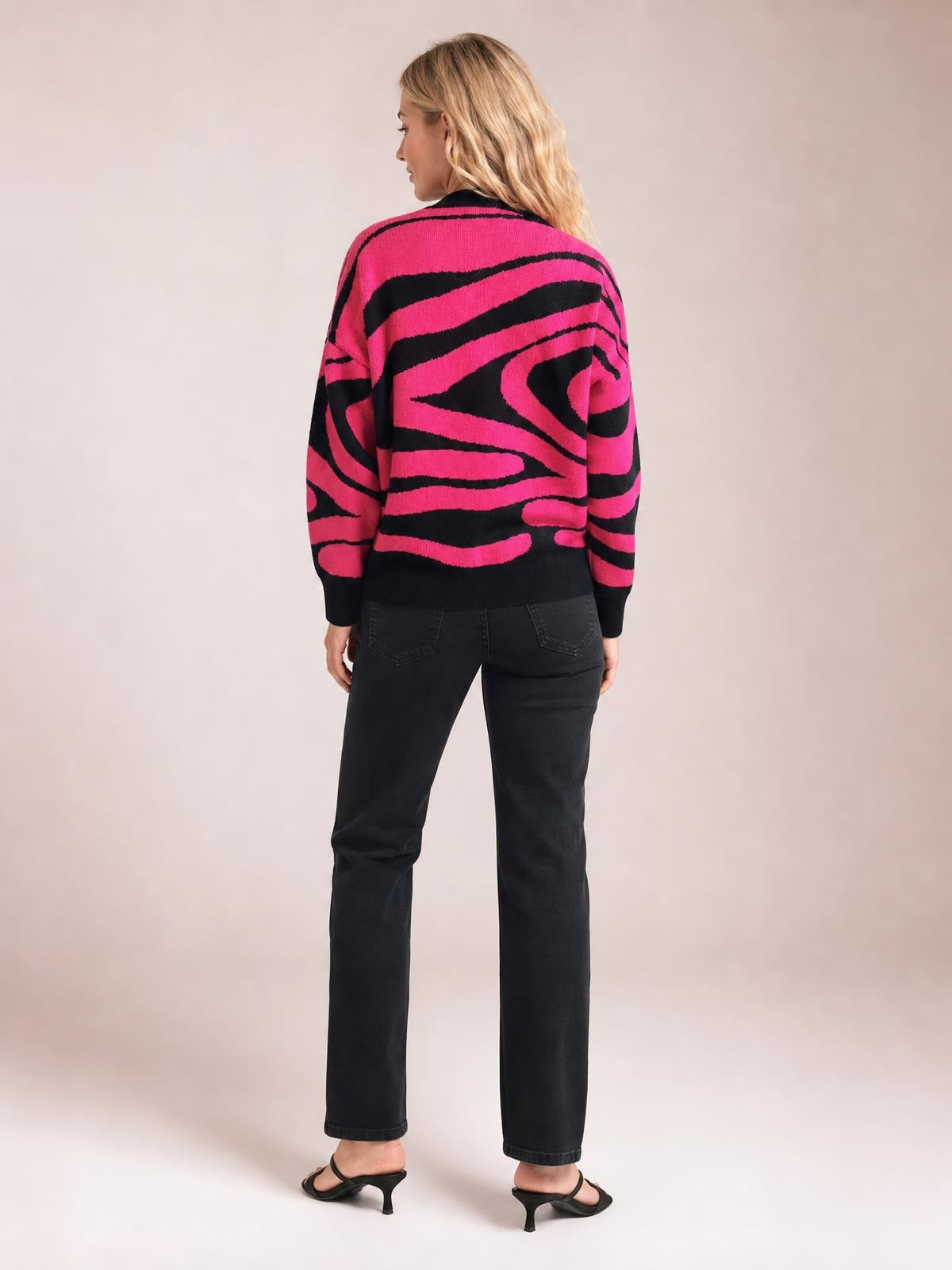 A model stands facing away in an oversized pink and black zebra print round neck sweater with long sleeves, ribbed cuffs, and a ribbed hem.