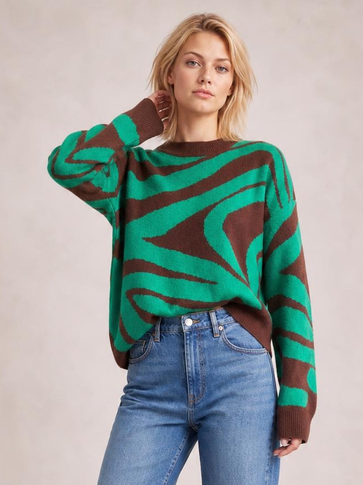 A model poses in an oversized zebra print sweater with a round brown ribbed neck, long sleeves, matching cuffs, and bold green and brown waves.