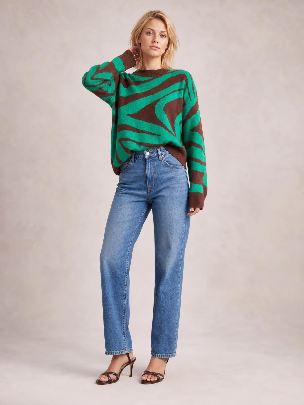 A model wears an oversized green and brown zebra-print round-neck sweater with long sleeves and ribbed trim, posing with one hand at her neck.