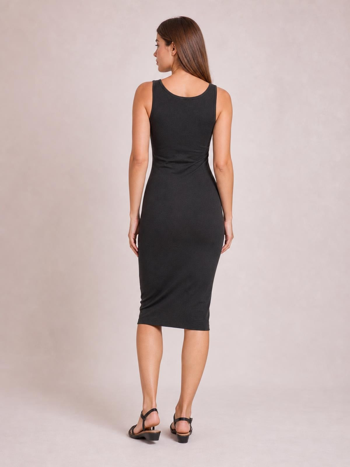Model viewed from behind in a black sleeveless cotton midi dress with a scoop back neckline, fitted bodycon silhouette, and clean hem.