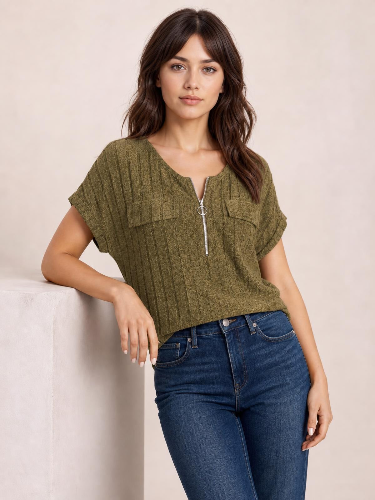 Model wearing an olive green ribbed short sleeve T-shirt with a relaxed silhouette, zip-front closure, chest pockets, and rolled cuffs while leaning casually.