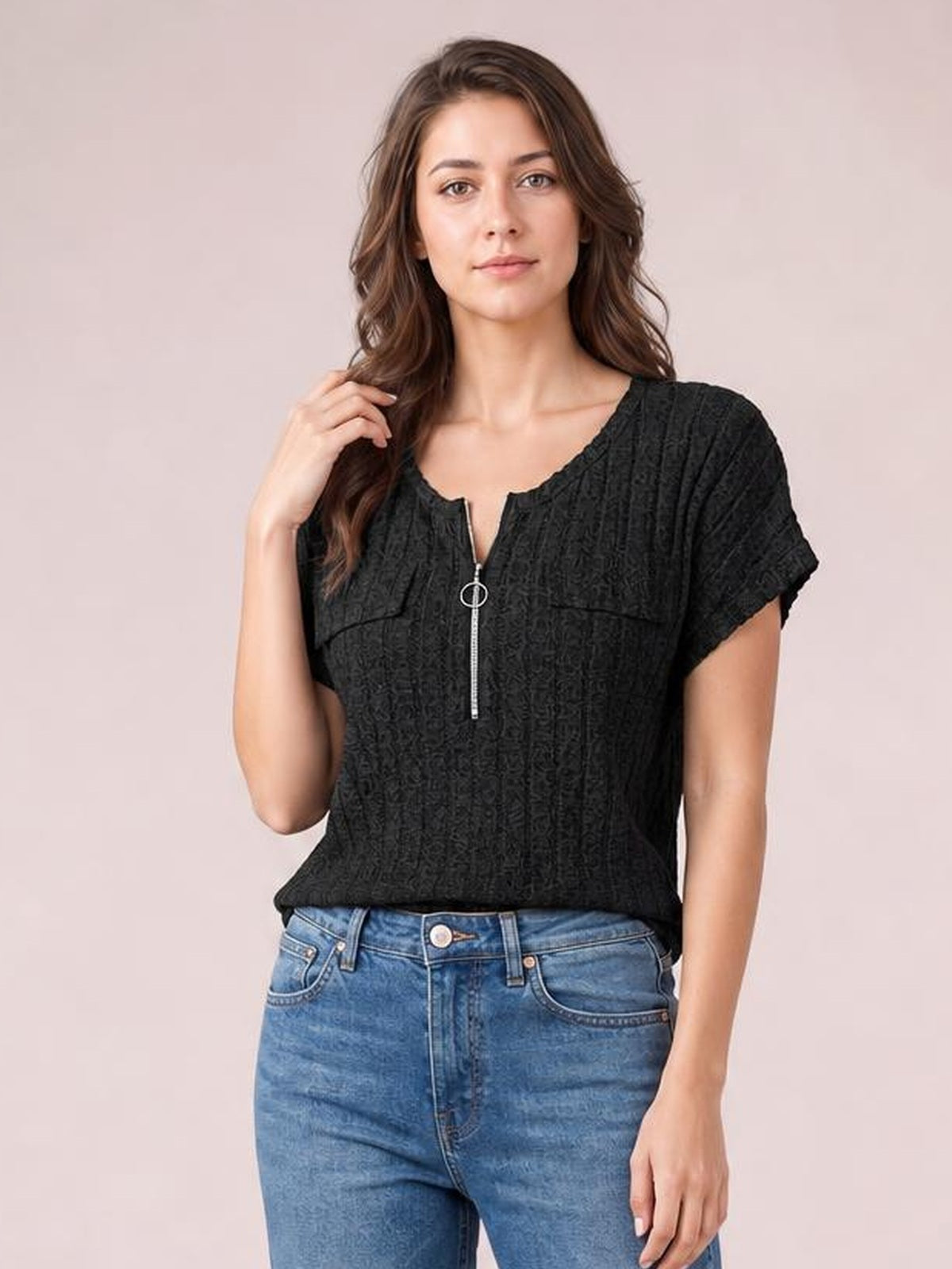 Model poses in a black ribbed short-sleeve T-shirt with a round neckline, half zip-front ring pull, and relaxed silhouette, one hand touching her hair.