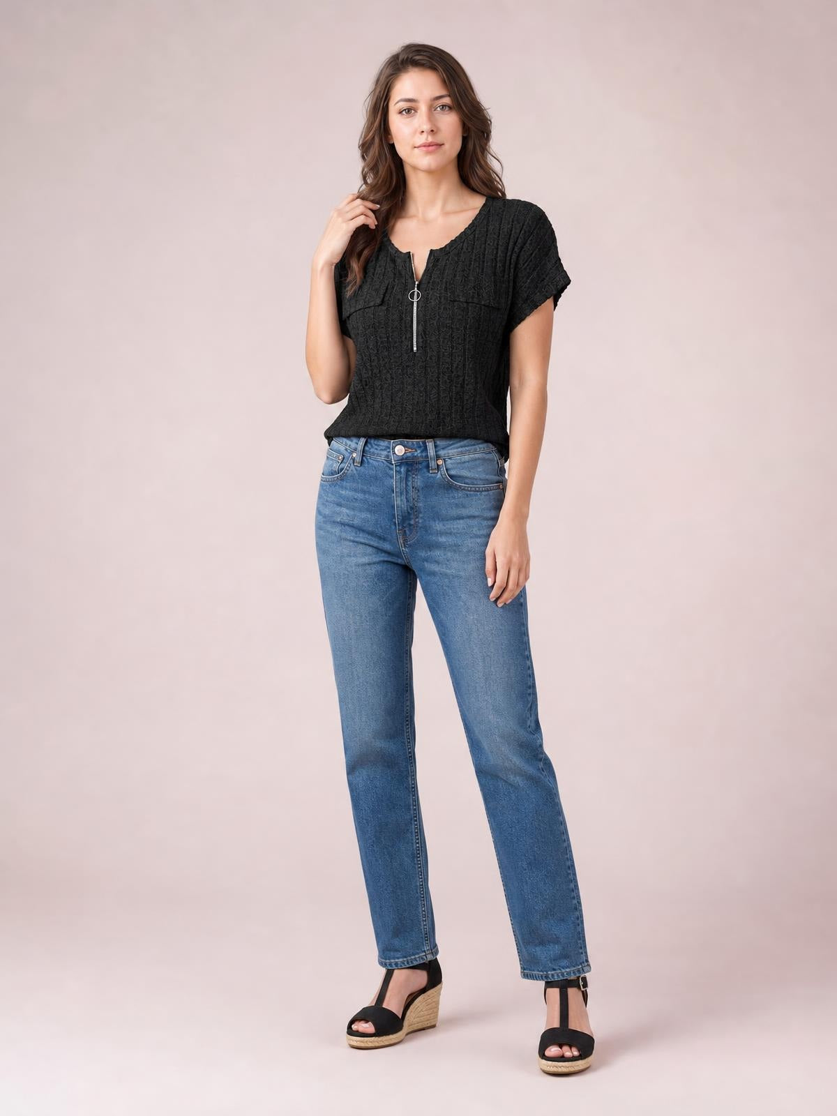 A model stands with one hand in her hair wearing a black ribbed short-sleeve T-shirt with a zip front, ring pull, and relaxed straight silhouette.