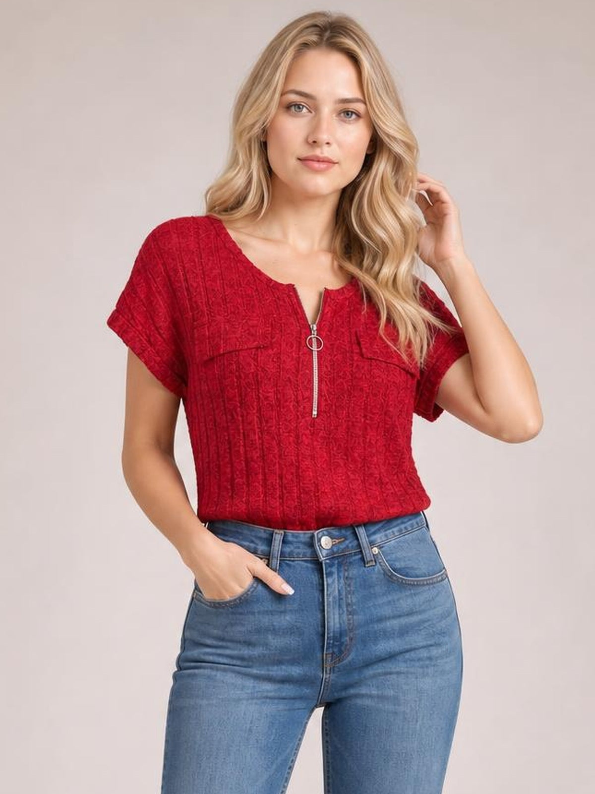 A model wears a red ribbed short sleeve T-shirt with a zip-front neckline and relaxed silhouette, posing with one hand in her jeans pocket.