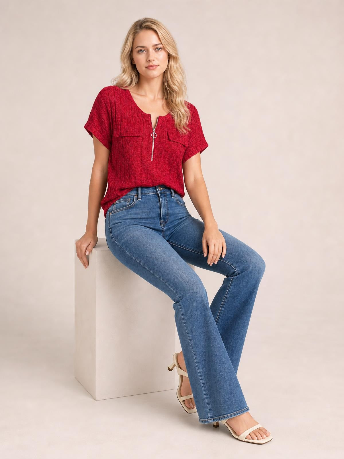 A seated model wears a red ribbed short-sleeve T-shirt with a zip-front neckline, relaxed silhouette, and visible front patch pockets.