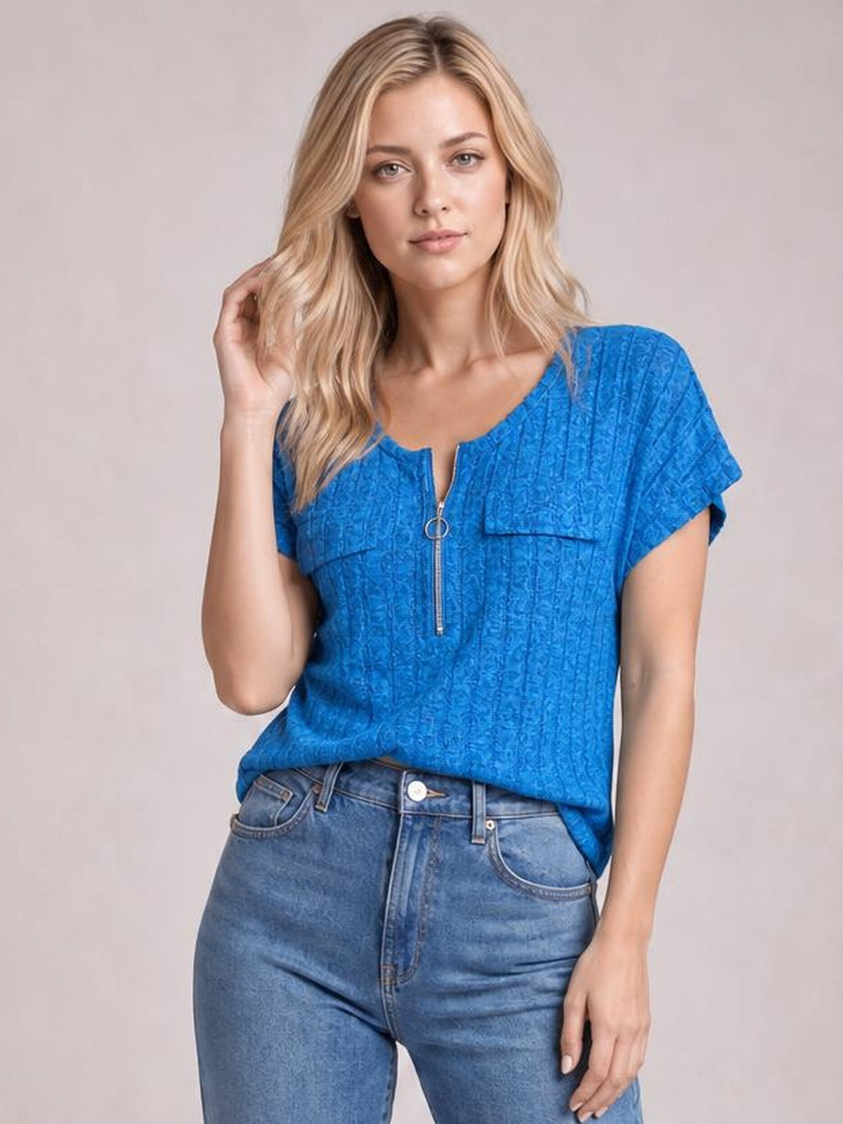 Model poses with one hand in her hair wearing a bright blue ribbed short-sleeve T-shirt with a front zipper and relaxed silhouette.