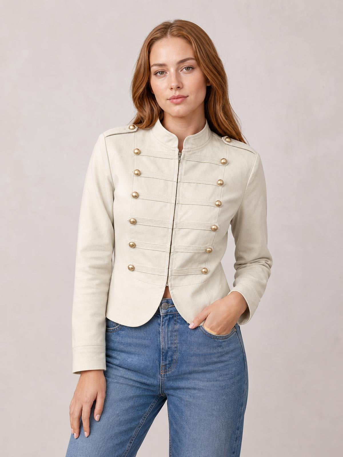 A model wears a cream cropped jacket with a zip front, stand collar, gold-tone buttons, long sleeves, and a fitted silhouette, posing with one hand in her pocket.