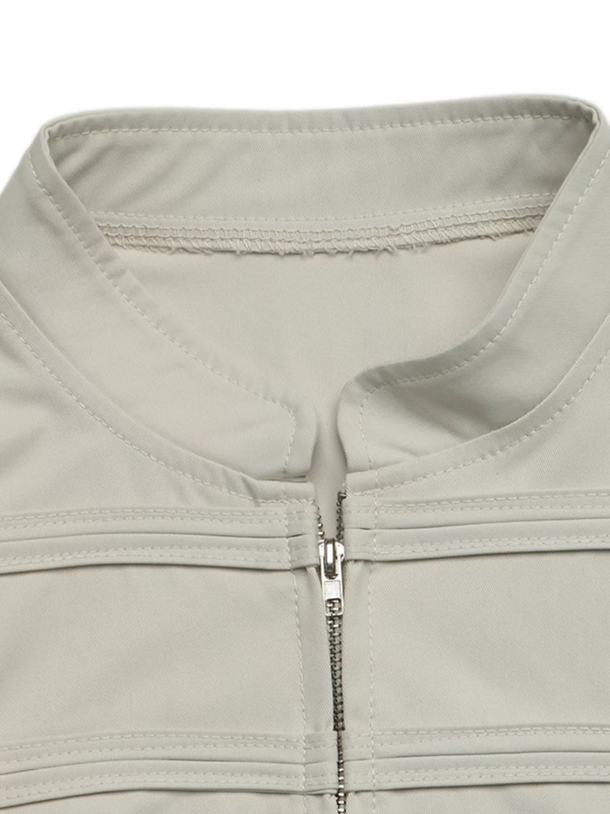 Close-up of a light gray cropped jacket showing its round neckline, front zip closure, reinforced seams, and smooth unlined construction.
