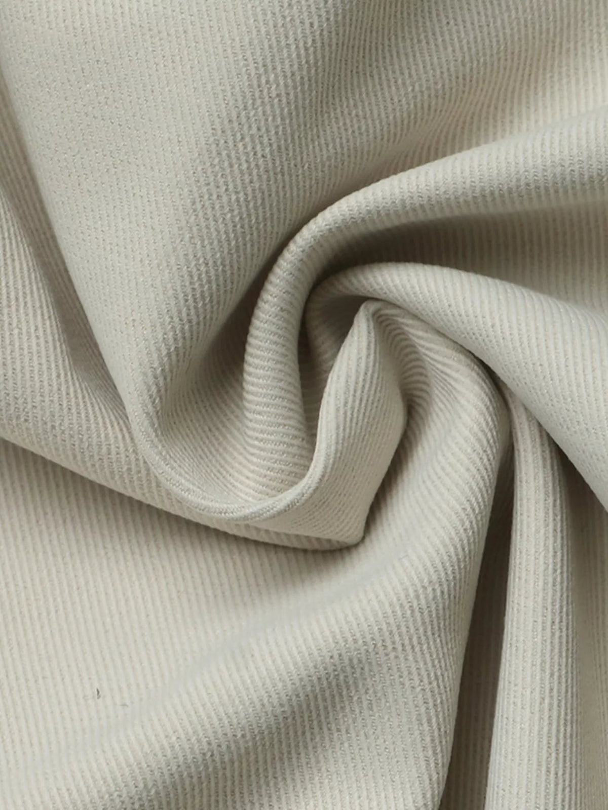Close-up of the cropped jacket’s soft cream fabric, showing fine vertical ribbing and folded construction details.