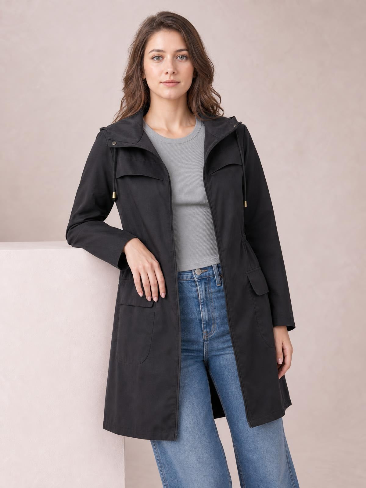 Model wearing a black zip-up hooded jacket with drawstring waist, long regular-fit silhouette, flap pockets, and a layered gray top with jeans.