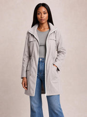 A woman stands in a light gray hooded jacket with an open zip front, drawstring waist, longline silhouette, flap chest pockets, and lower pockets.