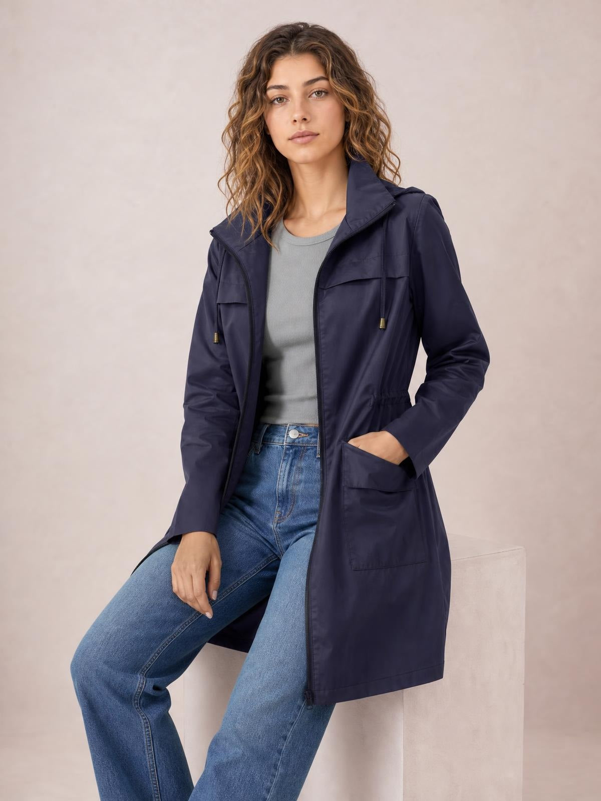 Model seated in a navy zip-up hooded jacket with drawstring waist, regular fit, long sleeves, and flap pockets.
