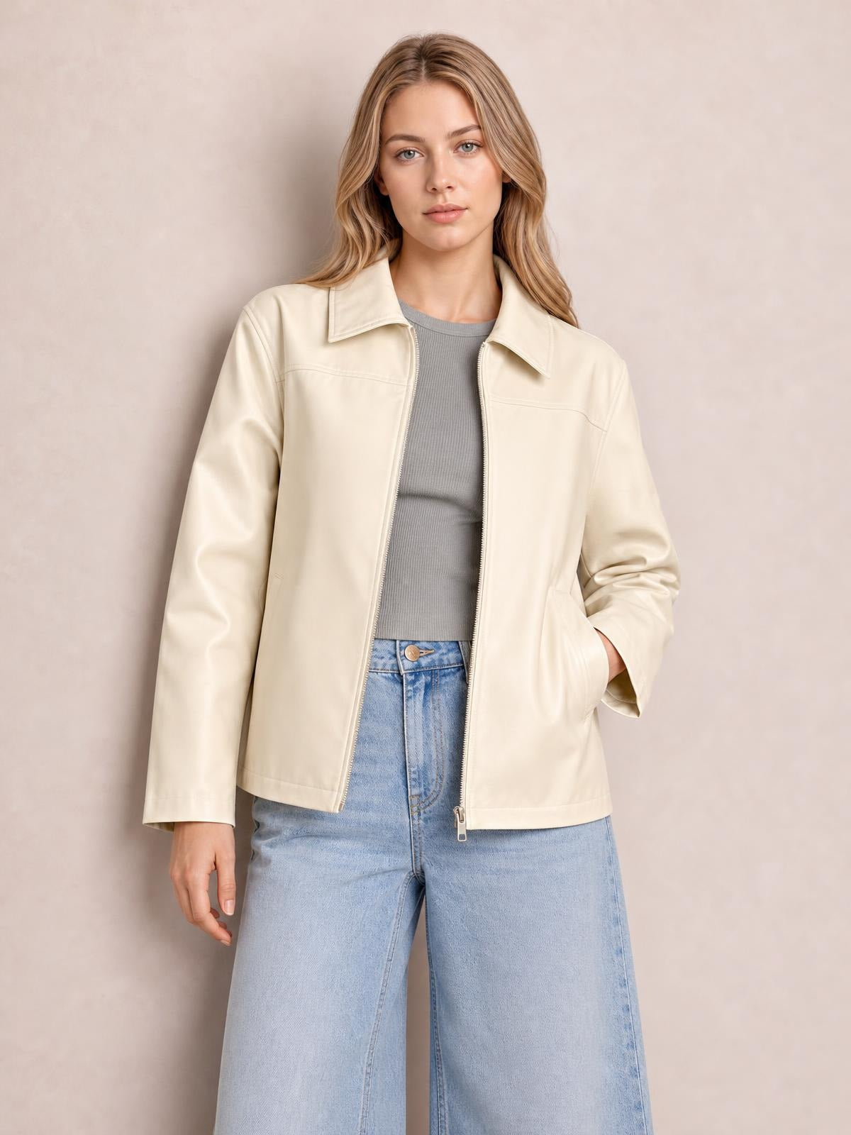 A model poses in a cream zip-up leather jacket with a collared neckline, long sleeves, straight silhouette, and side pockets, worn open over a gray top.