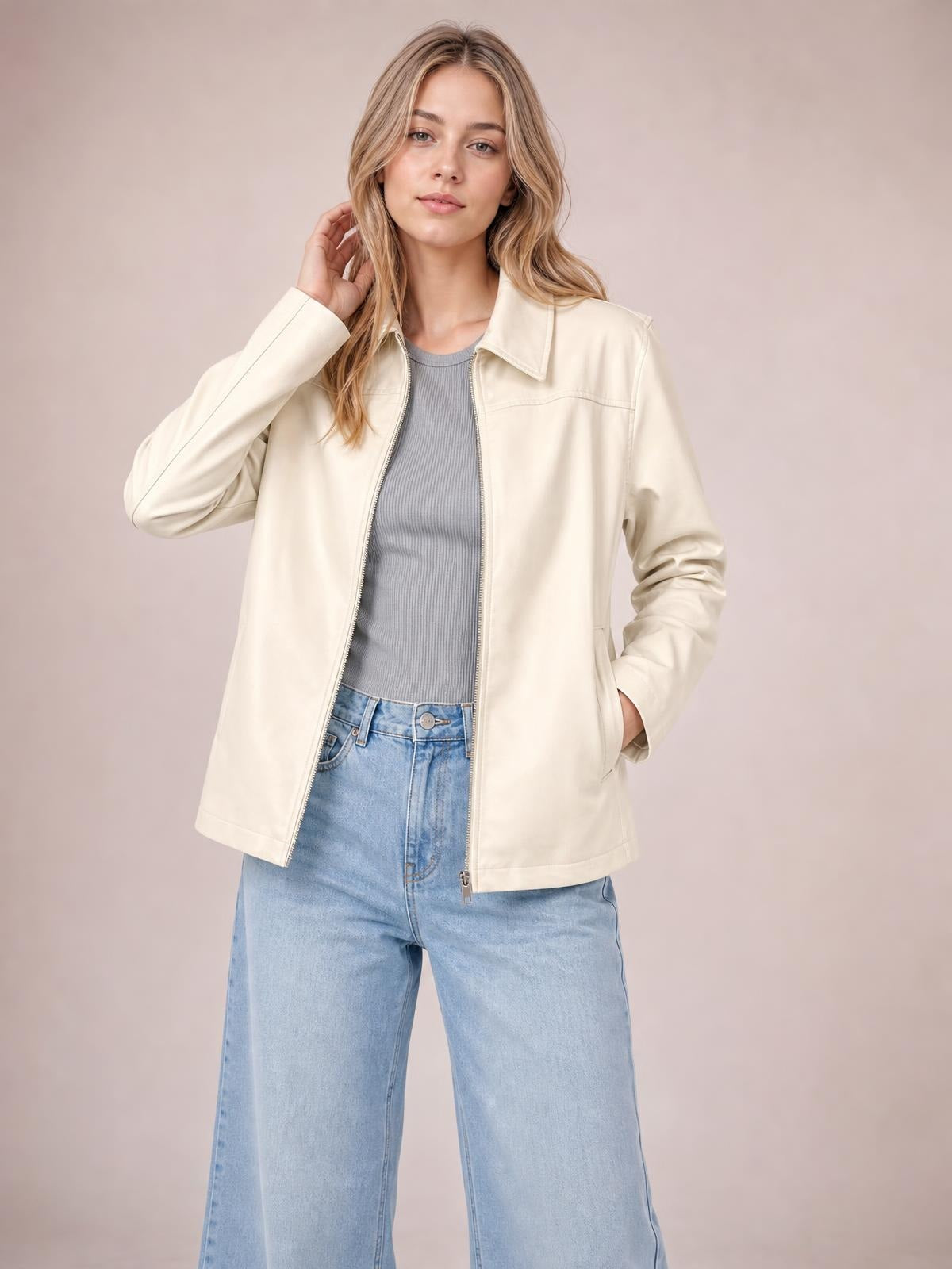 A model poses in a cream leather-look zip-up jacket with a pointed collar, long sleeves, relaxed silhouette, visible seam detailing, and side pockets.