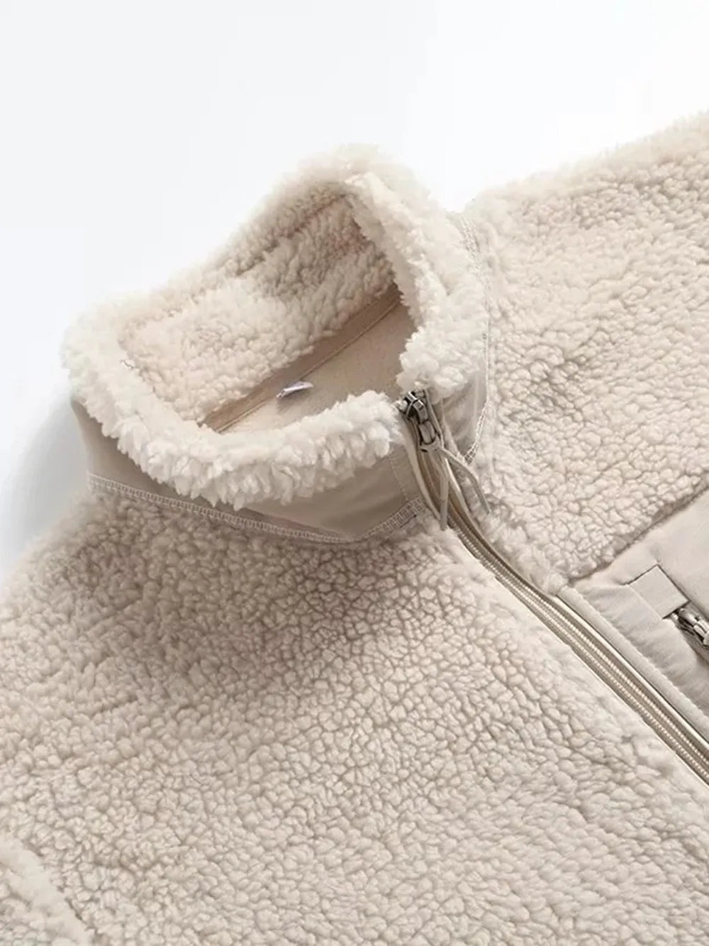 Close-up of a cream plush jacket showing its textured fleece, stand collar, zip-front closure, and long sleeve construction.