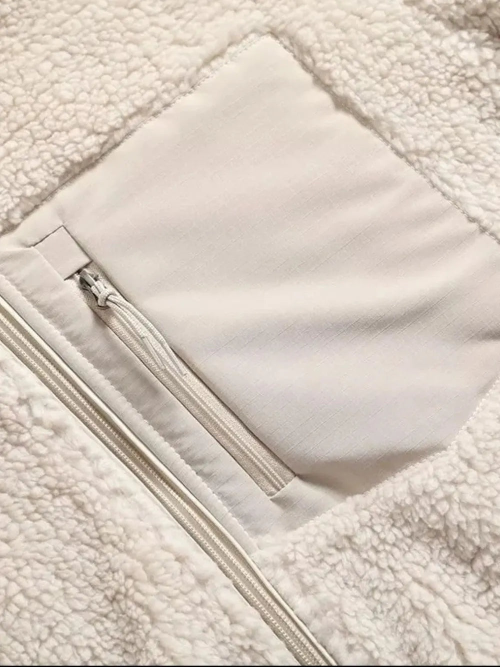 Close-up of an ivory plush jacket showing its soft textured fleece, long front zipper, and spacious unlined interior pocket.