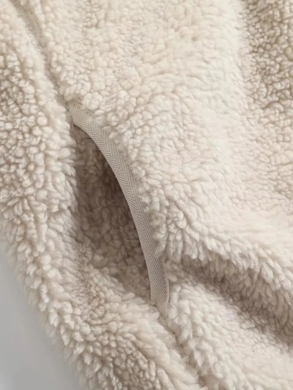 A close-up shows the cream plush jacket’s thick sherpa texture and neatly finished seam with contrasting herringbone binding.
