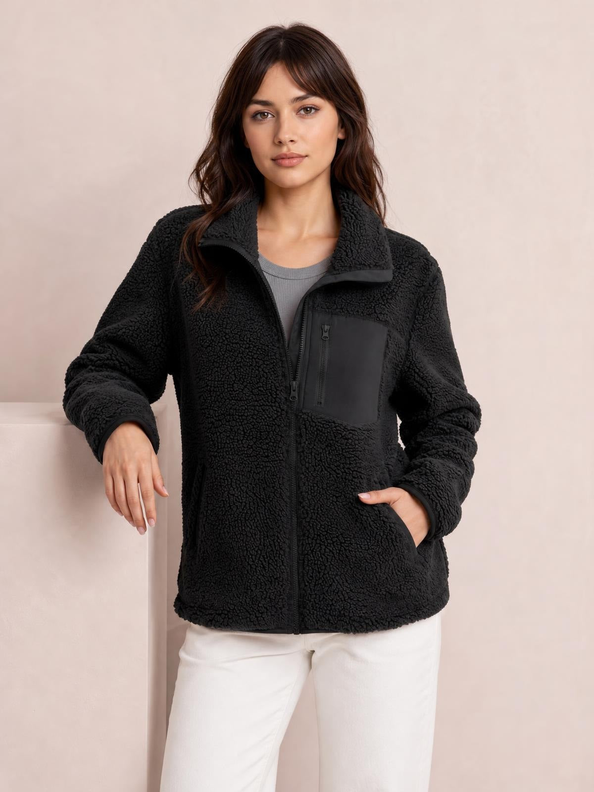 A model poses in a black plush long-sleeve jacket with a full front zip, stand collar, relaxed silhouette, zip chest pocket, and side hand pockets.