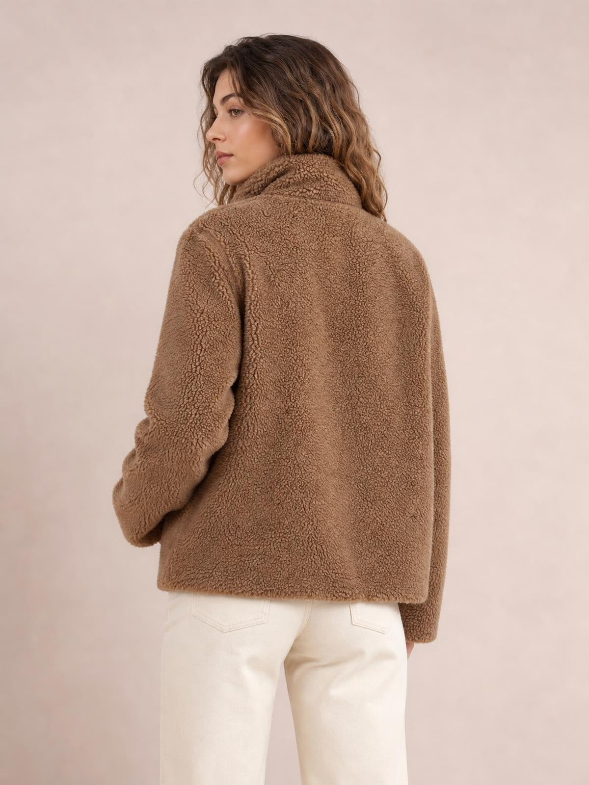 Model in a back three-quarter pose wears a brown plush zip-up jacket with long sleeves, a high collar, relaxed silhouette, and visible pocket.