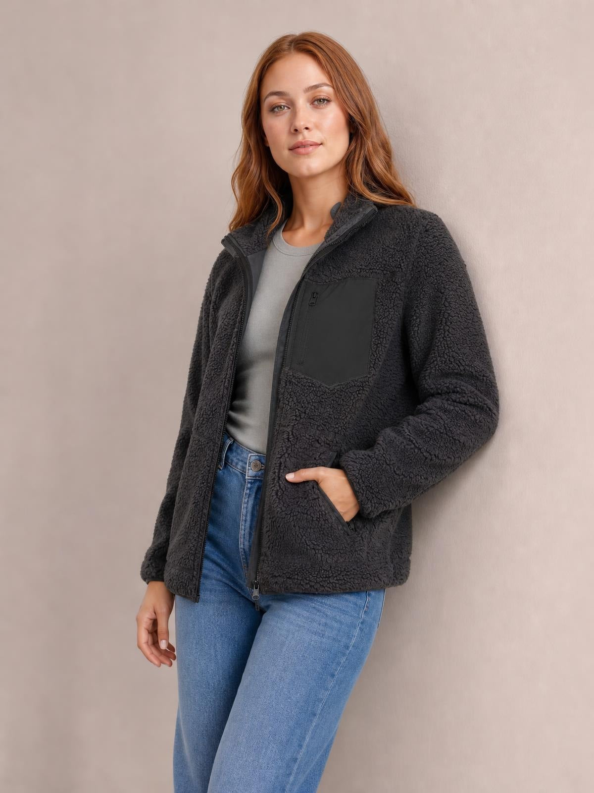 Model poses in a charcoal plush jacket with a zip front, long sleeves, stand collar, chest zip pocket, and side pockets, showing its relaxed silhouette.