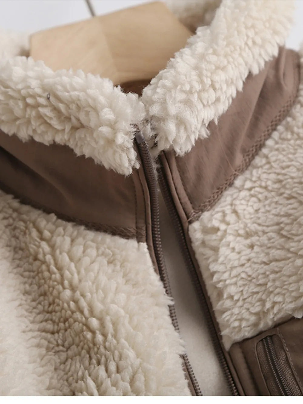 Close-up of a cream plush jacket with a brown zip front, soft sherpa texture, contrasting trim, and a visible zippered pocket.