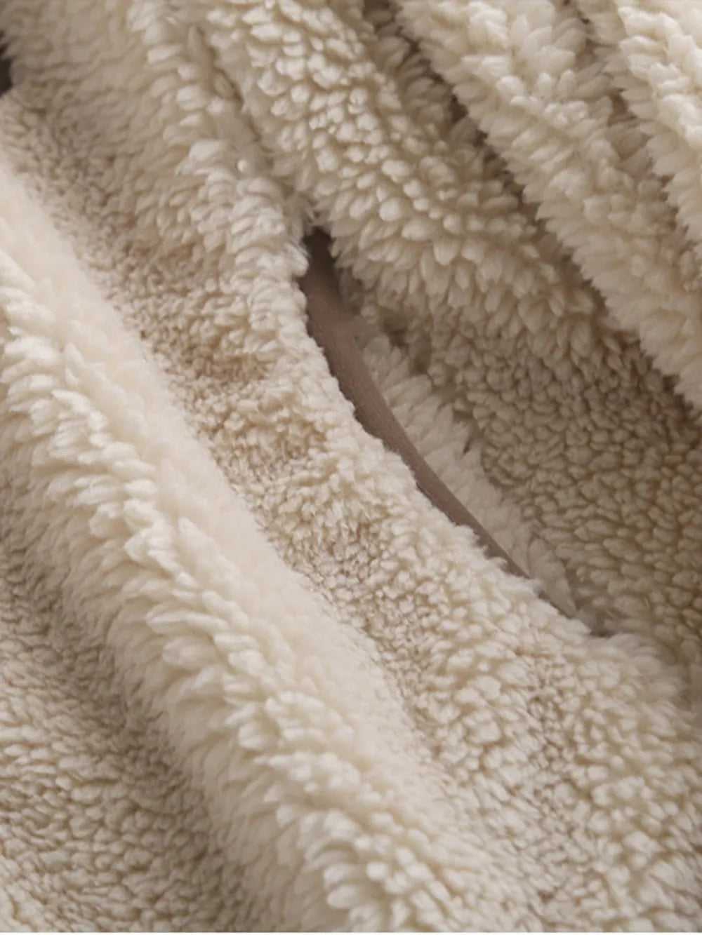 Close-up of a cream plush jacket fabric shows its thick, soft textured pile and folded construction detail.