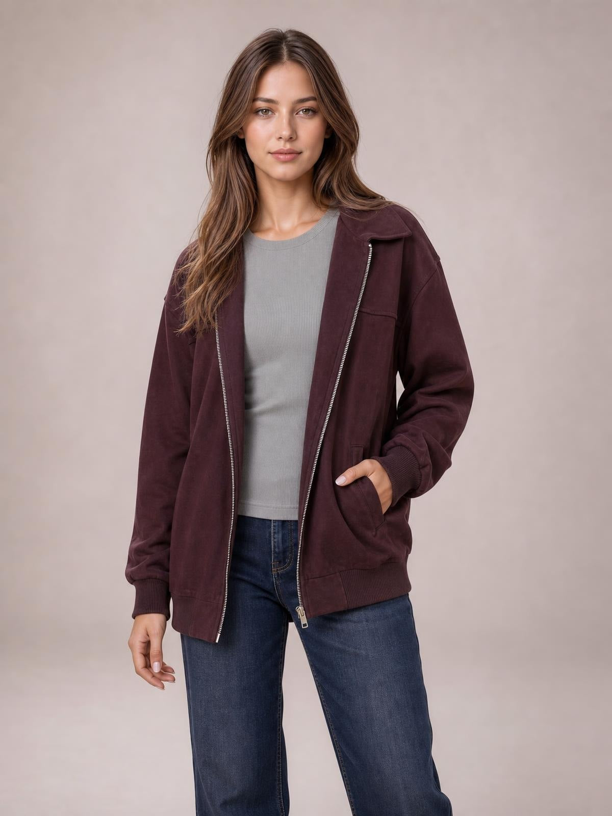 A model wears a burgundy zip-up jacket with a metal zipper, folded collar, long sleeves, ribbed cuffs and hem, and front pockets, posing with one hand tucked inside.
