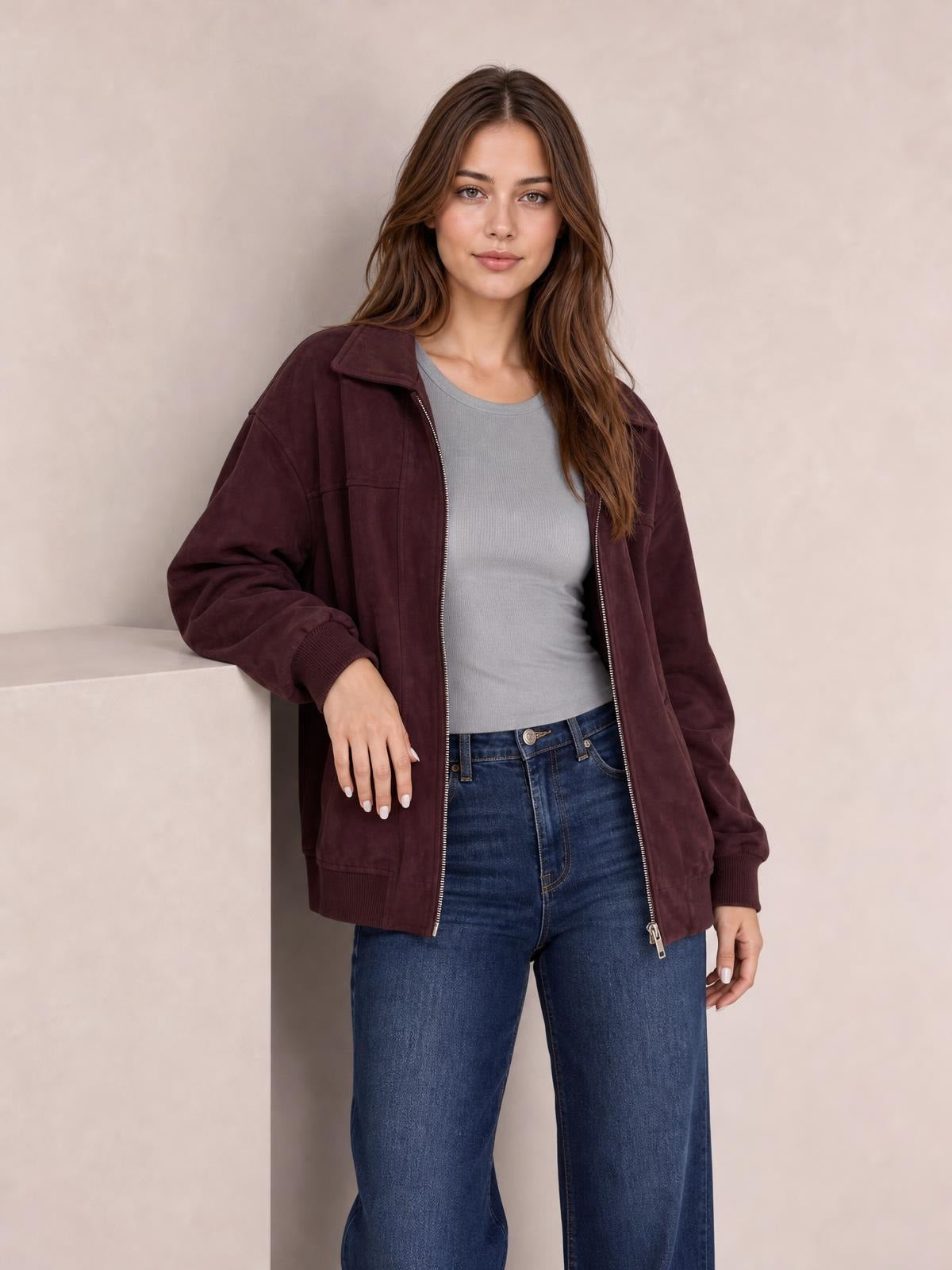 Model wears a burgundy zip-up jacket with a collar, long sleeves, ribbed cuffs, front pockets, and a relaxed silhouette while leaning casually.