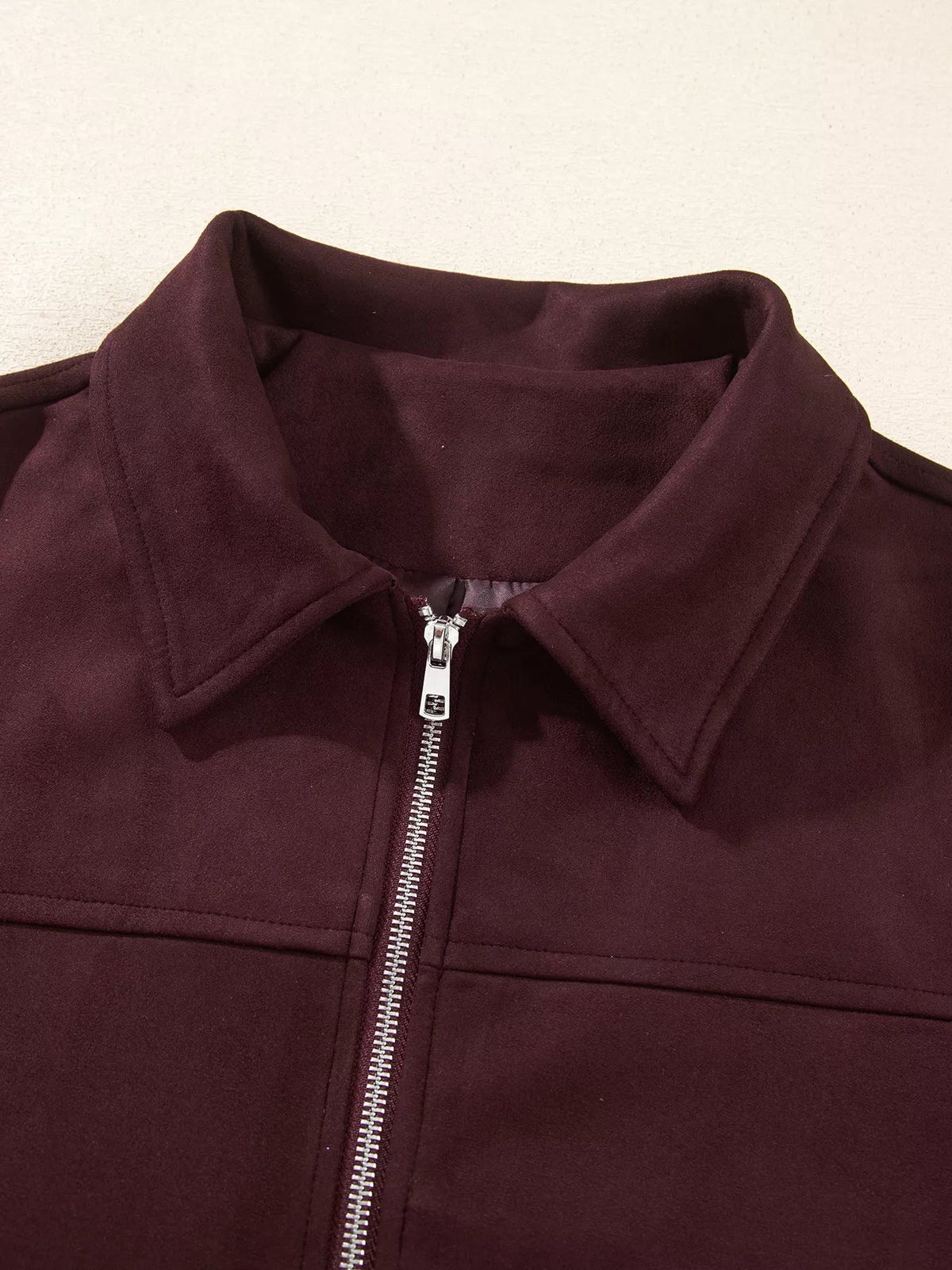 Close-up of a burgundy long-sleeve jacket showing its structured collar, silver metal zipper, clean seam construction, and smooth unlined body.