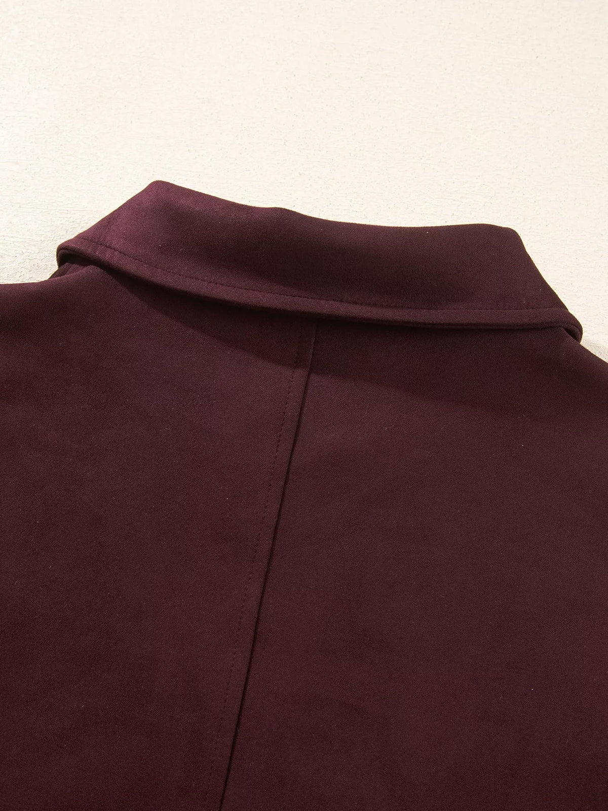 Close-up of a burgundy long-sleeve jacket showing its structured stand collar, smooth fabric, central front seam, and neat topstitching.