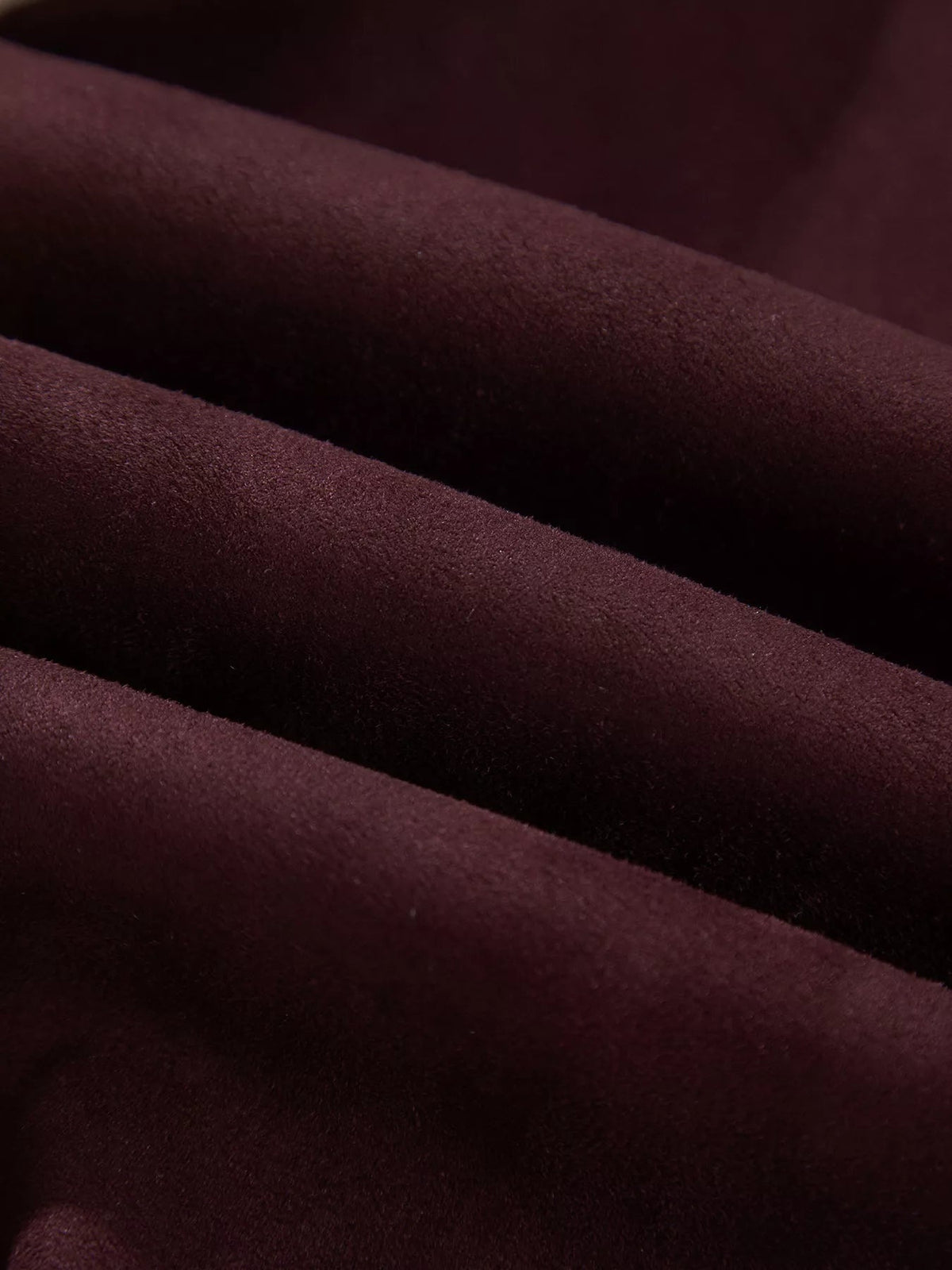Close-up of the jacket’s dark burgundy textured fabric, showing soft diagonal folds and a smooth, substantial surface without visible model or construction details.